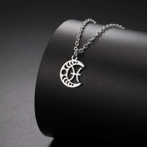 Gros plan d'un collier avec croissant de lune argenté et symbole du zodiaque Poissons