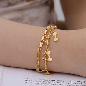 Detail of double-layer gold stainless steel bracelet with dumbbell pendant on wrist