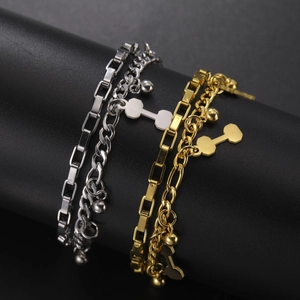 Detail view of stacked gold and silver stainless steel bracelets with dumbbell pendants