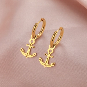 Detailed view of golden anchor-shaped earrings on elegant pink silk fabric background