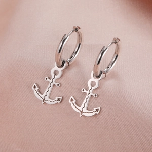 Macro shot of silver anchor drop earrings with wave patterns on soft pink satin fabric
