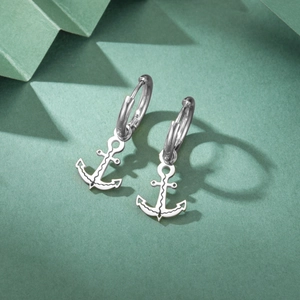 Macro view of geometric silver anchor pendant earrings on a soft green background