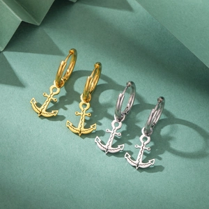 Detail view of gold and silver anchor pendant earrings on dark green background