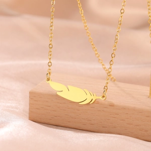 Close-up of golden feather pendant necklace on pink silk and light wood background