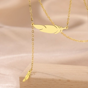 Detail view of a 18K gold-plated feather pendant necklace on a beige silk fabric background