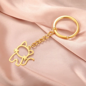 Détail du porte-clés chat évidé en métal doré poli sur fond de soie rose élégant