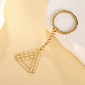 Detail of a golden geometric hollow triangle keychain on a white decorative stone base