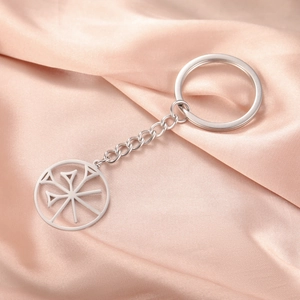 Detail of silver stainless steel keychain with round hollow geometric symbol on silk fabric