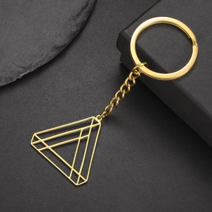 Macro shot of gold geometric triangle keychain with metallic luster on dark rock surface
