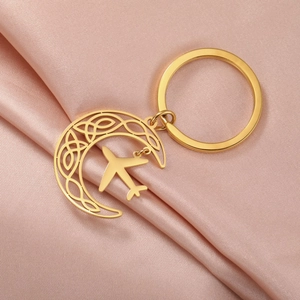 Detail of golden moon keychain with Celtic knot and airplane charm on satin background