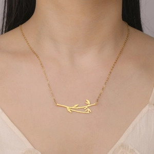 Close-up of a gold bamboo pendant necklace with detailed leaves on a female model