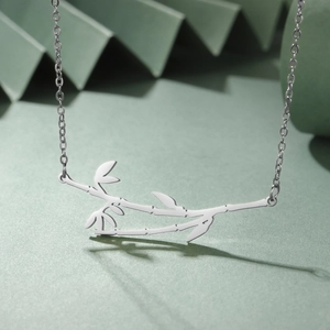 Detailed view of silver bamboo pendant necklace on a green textured background