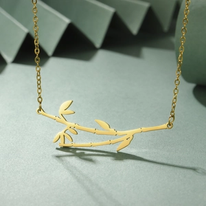 Detailed view of a gold bamboo leaf pendant necklace on a premium green background