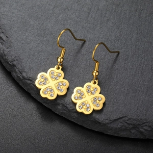Boucles d'oreilles trèfle dorées avec pétales en cœur et cristaux sur fond pierre