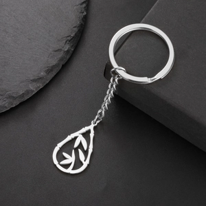 Polished silver teardrop bamboo leaf pendant keychain on textured dark stone background