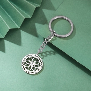 Detail of silver stainless steel keychain with hollow geometric flower pendant on green paper