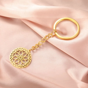 Macro shot of gold stainless steel mandala flower keychain on soft pink silk background