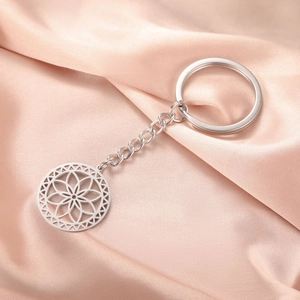 Macro shot of silver stainless steel keychain with hollow floral mandala pendant on silk