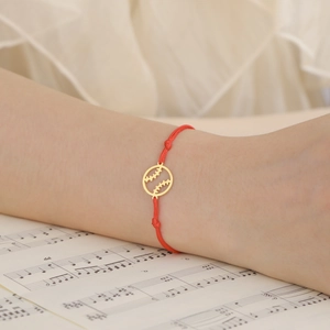 Detail van rood gevlochten touwarmband met gouden honkbal hanger om de pols gedragen
