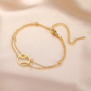 Nahaufnahme eines goldenen Edelstahl-Armbands, zweilagig mit Baseball-Anhänger und Perlen