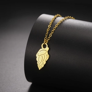 Detail of a gold conch pendant on a black pedestal showcasing fine carved metal texture