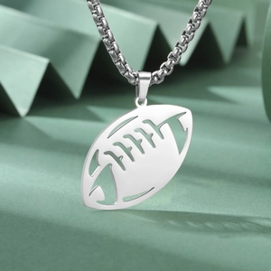 Détail d'un pendentif de rugby argenté avec chaîne à mailles sur fond vert