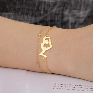 Detail of a double-layered gold stainless steel bracelet with a yoga pendant on a wrist