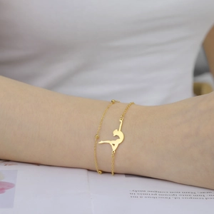 Detail of a gold double-layer chain bracelet featuring a dancer silhouette and small beads