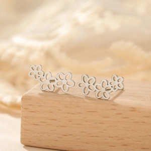 Dettaglio di tre orecchini a lobo a margherita in acciaio inossidabile su base in legno