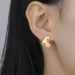 Close-up of golden ice skate stud earring worn on ear showing fine detail and size