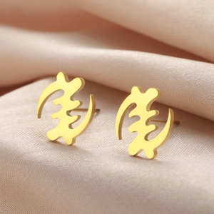Makroansicht goldener Gye Nyame Symbol-Ohrstecker auf pinkfarbenem Seidenhintergrund