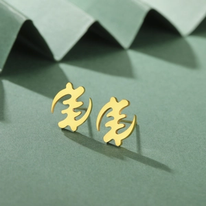Makro-Detail von goldenen Gye Nyame Adinkra Symbol Ohrringen aus rostfreiem Edelstahl
