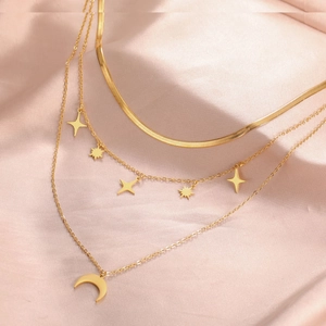 Detalle de collar dorado de varias capas con estrella y luna sobre raso rosa