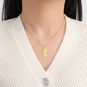 Detalle de un collar de acero inoxidable dorado con dos colgantes de huellas sobre una modelo