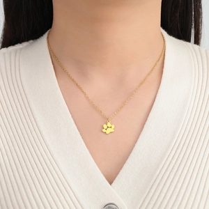 Primer plano del collar con colgante de huella de gato en acero dorado sobre ropa a rayas