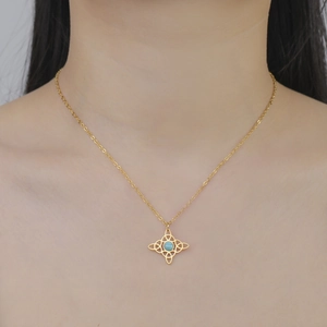 Close-up of a gold Celtic knot necklace with a turquoise bead on a model's neck