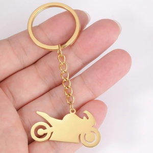 Close-up of a gold-toned motorcycle silhouette keychain held in hand with a white background