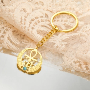 Dettaglio di un ciondolo Ankh dorato con ali e perla turchese su pizzo beige