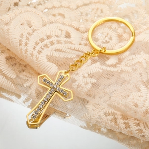 Close-up of golden cross keychain with sparkling rhinestones on elegant lace background