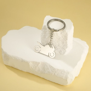 Polished silver motorcycle pendant keychain displayed on a white stone textured surface