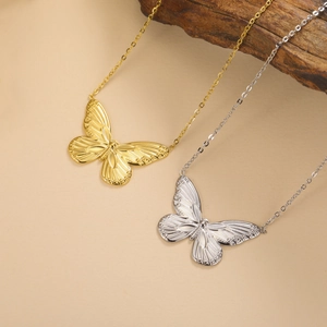 Elegante Halsketten mit Schmetterlingsanhänger in Gold und Silber auf beigem Hintergrund.