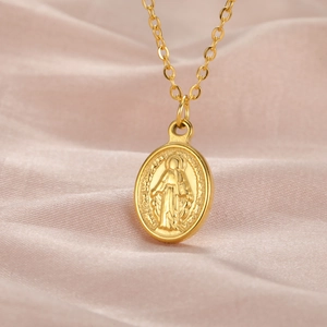 Close-up of gold stainless steel oval pendant with Virgin Mary relief on pink silk