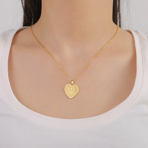 Detail of a gold heart pendant necklace with LIL SIS engraving on a O-chain link