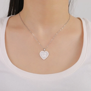 Detail showing a silver heart pendant engraved with LIL SIS on a minimalist chain
