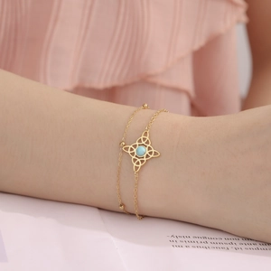Nahaufnahme eines goldenen keltischen Knotens am Doppelarmband mit blauer Perle am Handgelenk