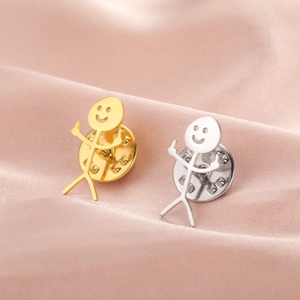 Close-up of funny stickman pins in gold and silver finish on soft satin fabric
