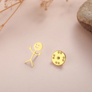 Detail of funny gold stickman brooch with smile and middle finger on pink background