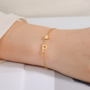 Detail eines goldenen Edelstahl-Kettenarmbands mit Herz- und Buchstaben-P-Anhängern
