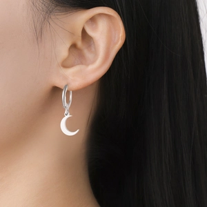Close-up of a silver stainless steel crescent moon pendant earring worn by a model