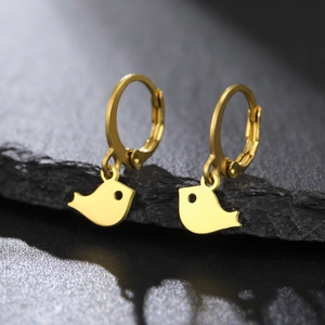 Détail macro de boucles d'oreilles oiseaux en or poli posées sur une pierre naturelle noire